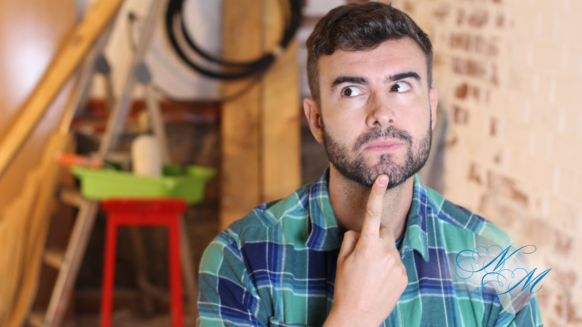 Man with beard, eyes crossed, finger on chin, pondering in a construction area with tools and brick wall.