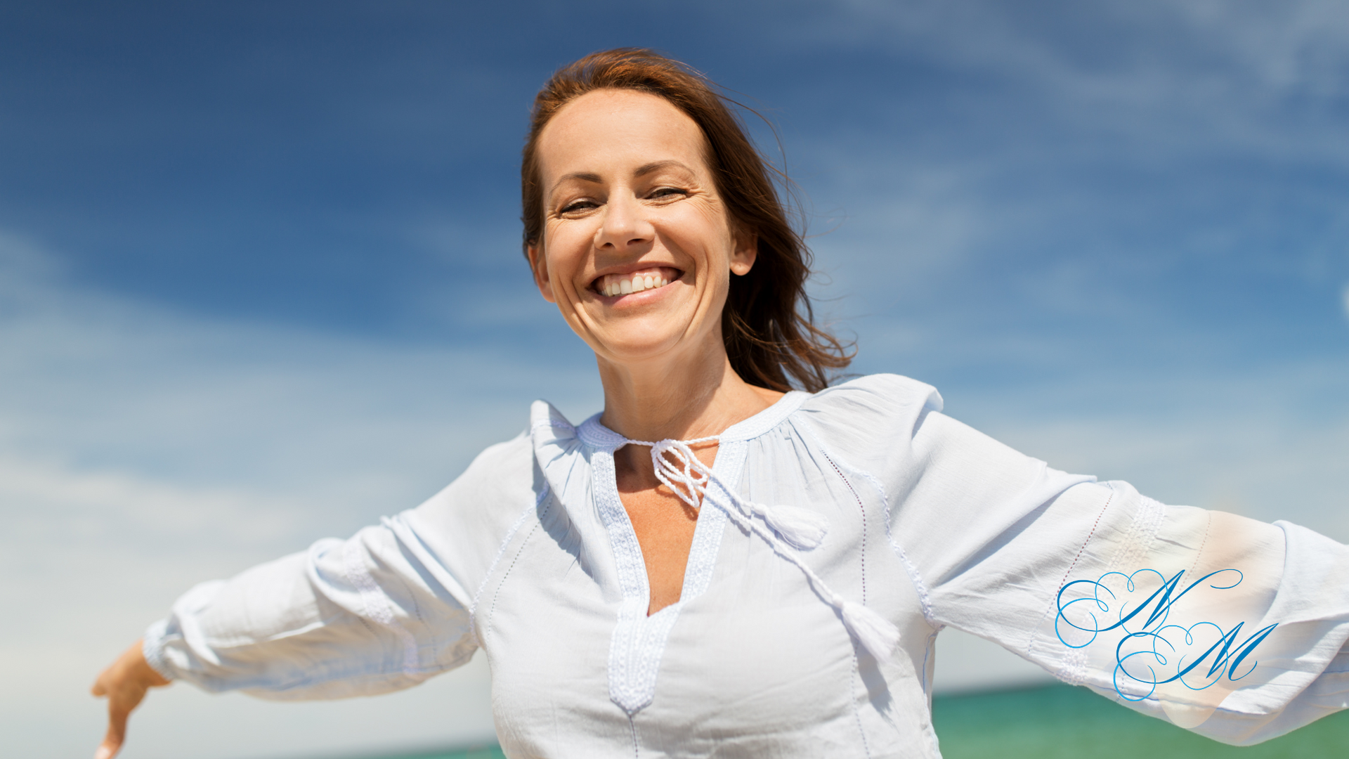 A woman is standing on the beach with her arms outstretched and smiling.