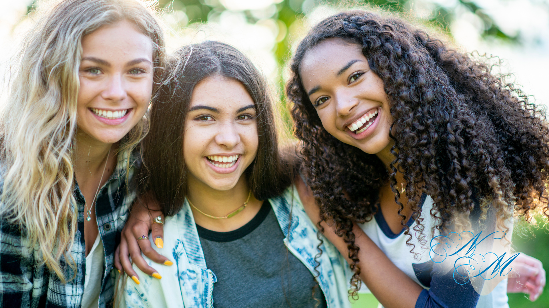 Four smiling people huddle together under a blue sky, arms around each other, looking down.