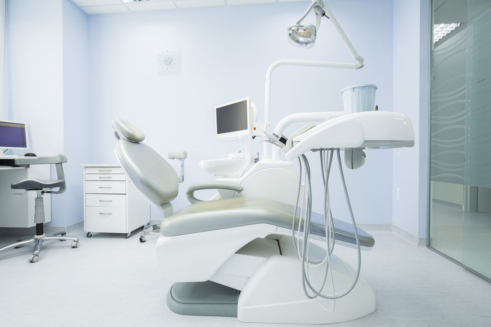 An empty dental office with a dental chair and a computer.