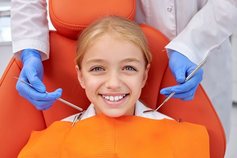 A little girl is sitting in a dental chair while a dentist examines her teeth.