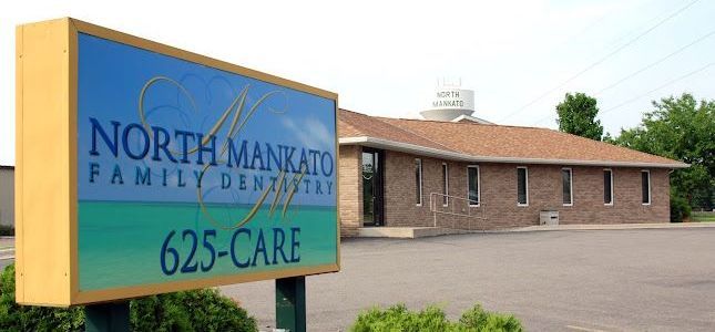 A sign for north mankato family dentistry is in front of a brick building