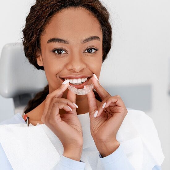 A woman is smiling while holding a dental retainer in her mouth.