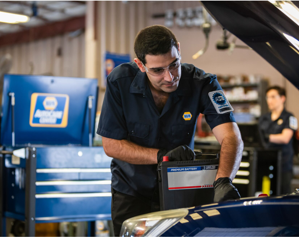 Mechanic replacing a car battery at NAPA Auto Parts. Man in blue uniform, holding battery, focused | Jim's Auto Repair & Towing