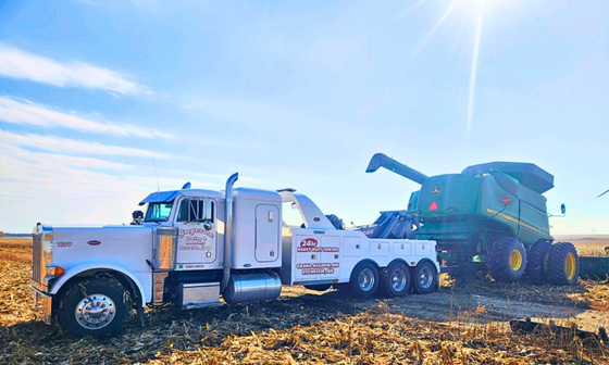 A tow truck is towing a combine harvester in a field.