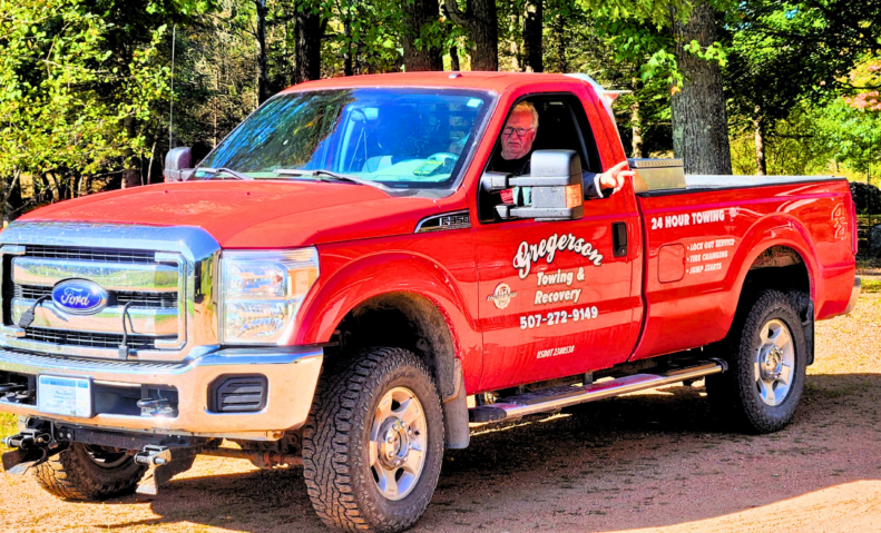 A red pickup truck is parked on a dirt road.