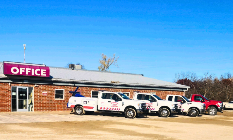 A row of trucks are parked in front of a building that says office.