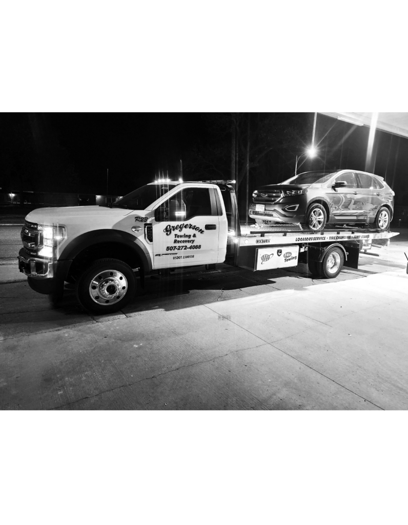 A black and white photo of a tow truck carrying a car.