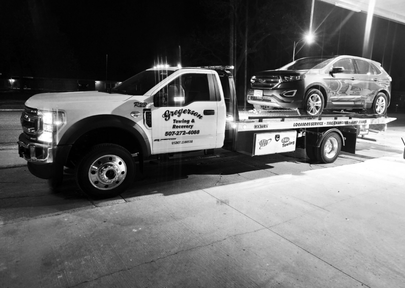 A black and white photo of a tow truck with a car on the back.