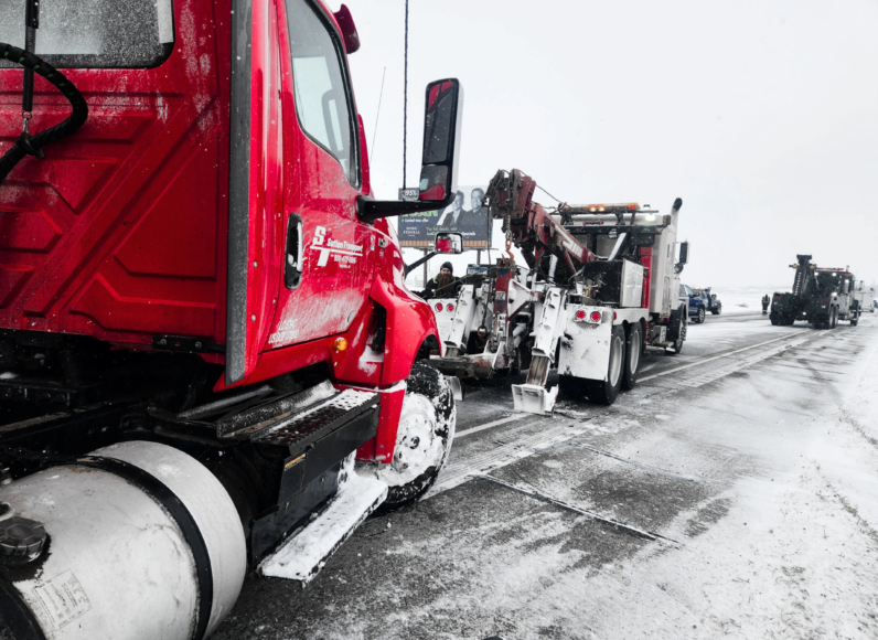 A red tow truck is sitting on the side of the road next to a white tow truck.