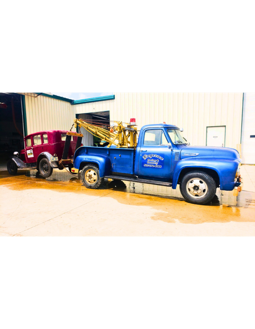 A blue tow truck is towing a red car.