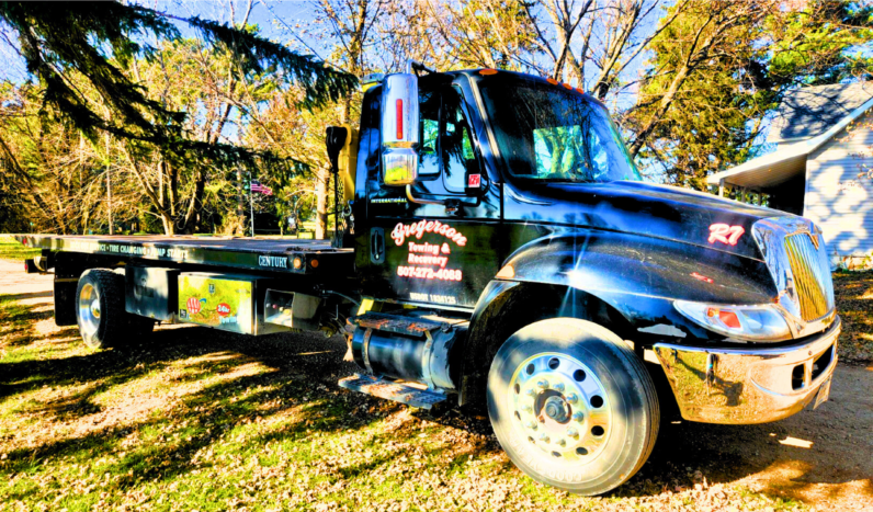 A tow truck is parked in the grass in front of a house.