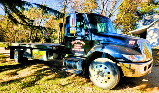A tow truck is parked in the grass in front of a house.