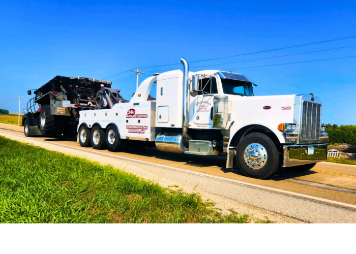 A white tow truck is driving down a dirt road.