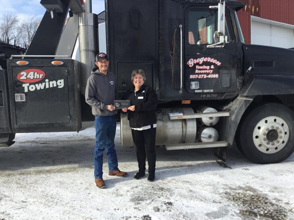 A man and a woman are standing in front of a towing truck.