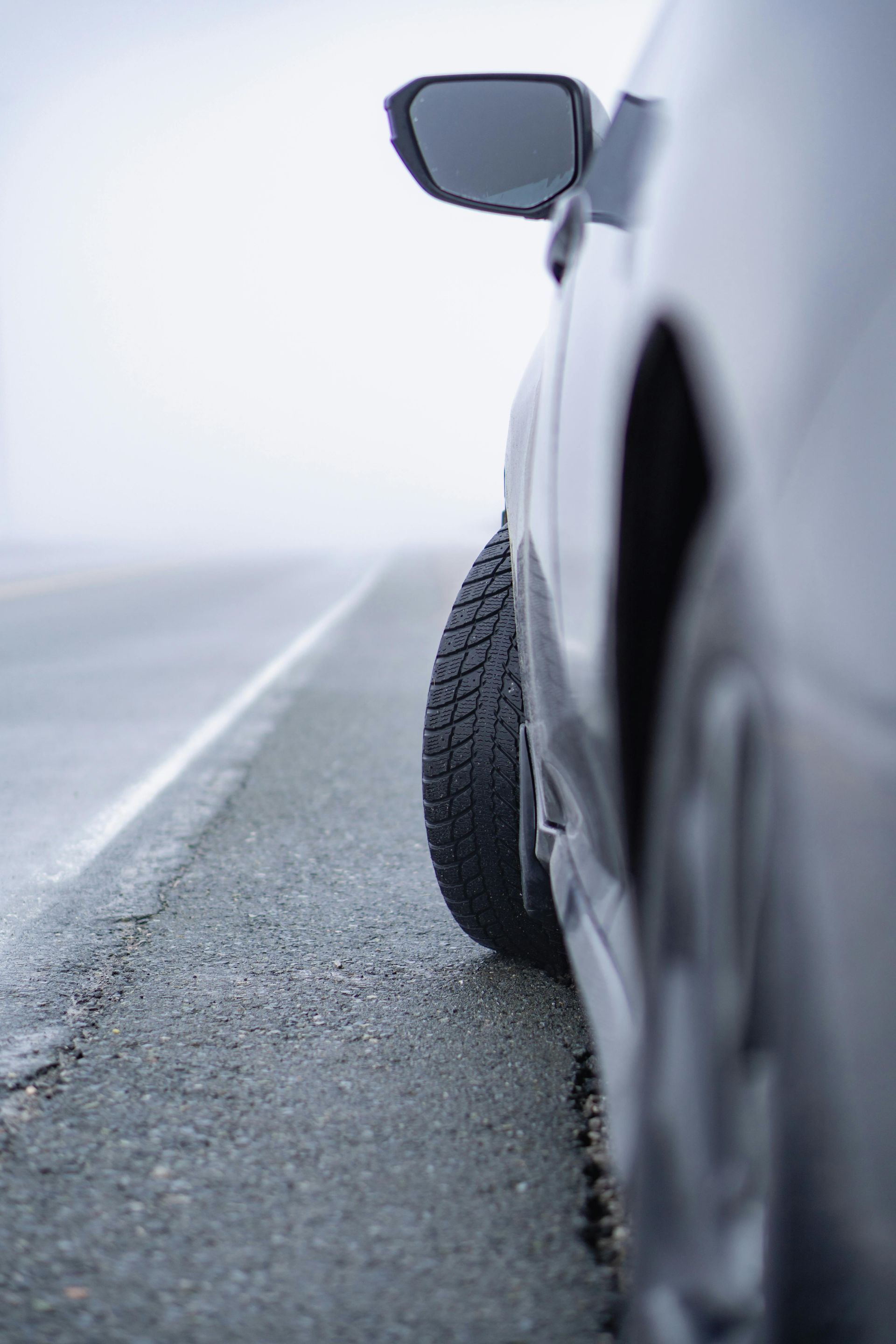 Close-up, low-angle view of a car parked on the shoulder of a road in thick fog.