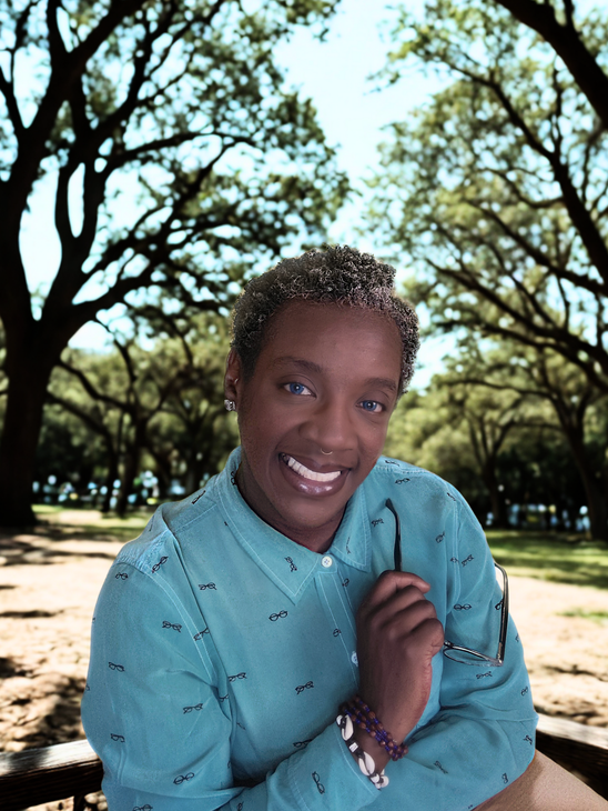 Person working at a light wood desk with books, plants, and vase of eucalyptus. White chair and walls.