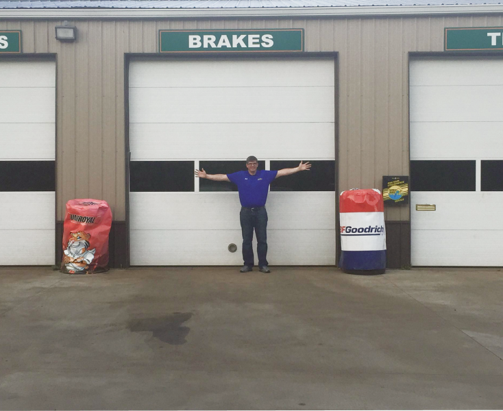 A person in a blue shirt stands with arms wide in front of a garage bay door labeled 