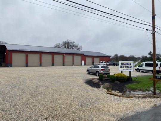 A black-and-white photo of a person in a plaid shirt, hand to their face, leaning against a brick wall.