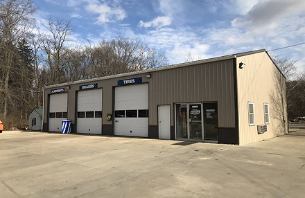 A beige, single-story metal commercial building with three garage bays and a side entrance in a paved, open-air lot.