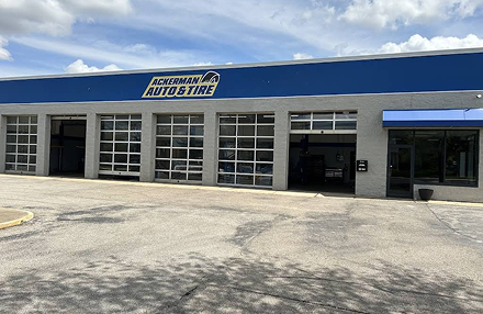 Ackerman Auto & Tire repair shop with a blue sign, grey exterior, multiple garage bays, and a front glass entrance.