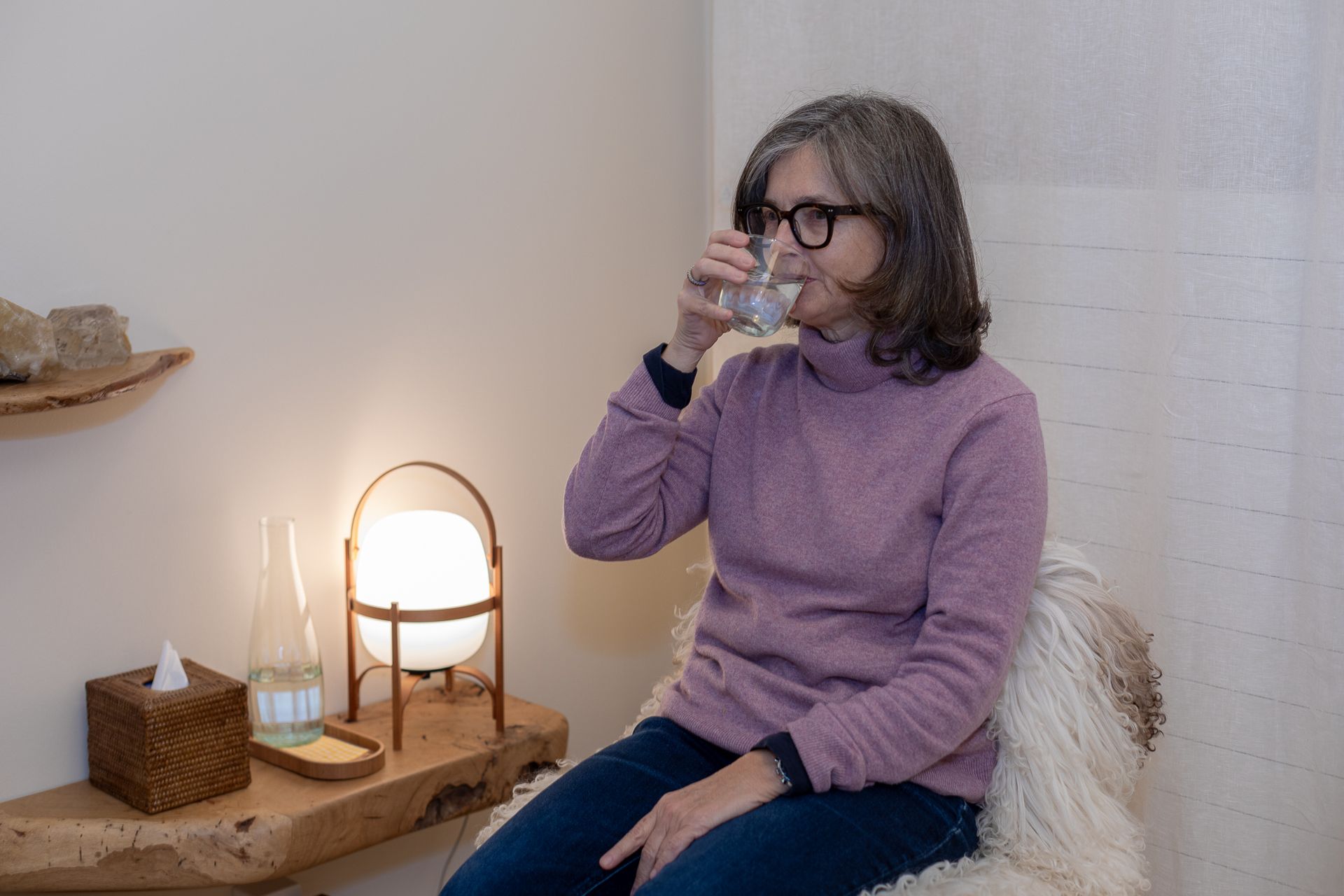 A woman is sitting in a chair drinking a glass of water.