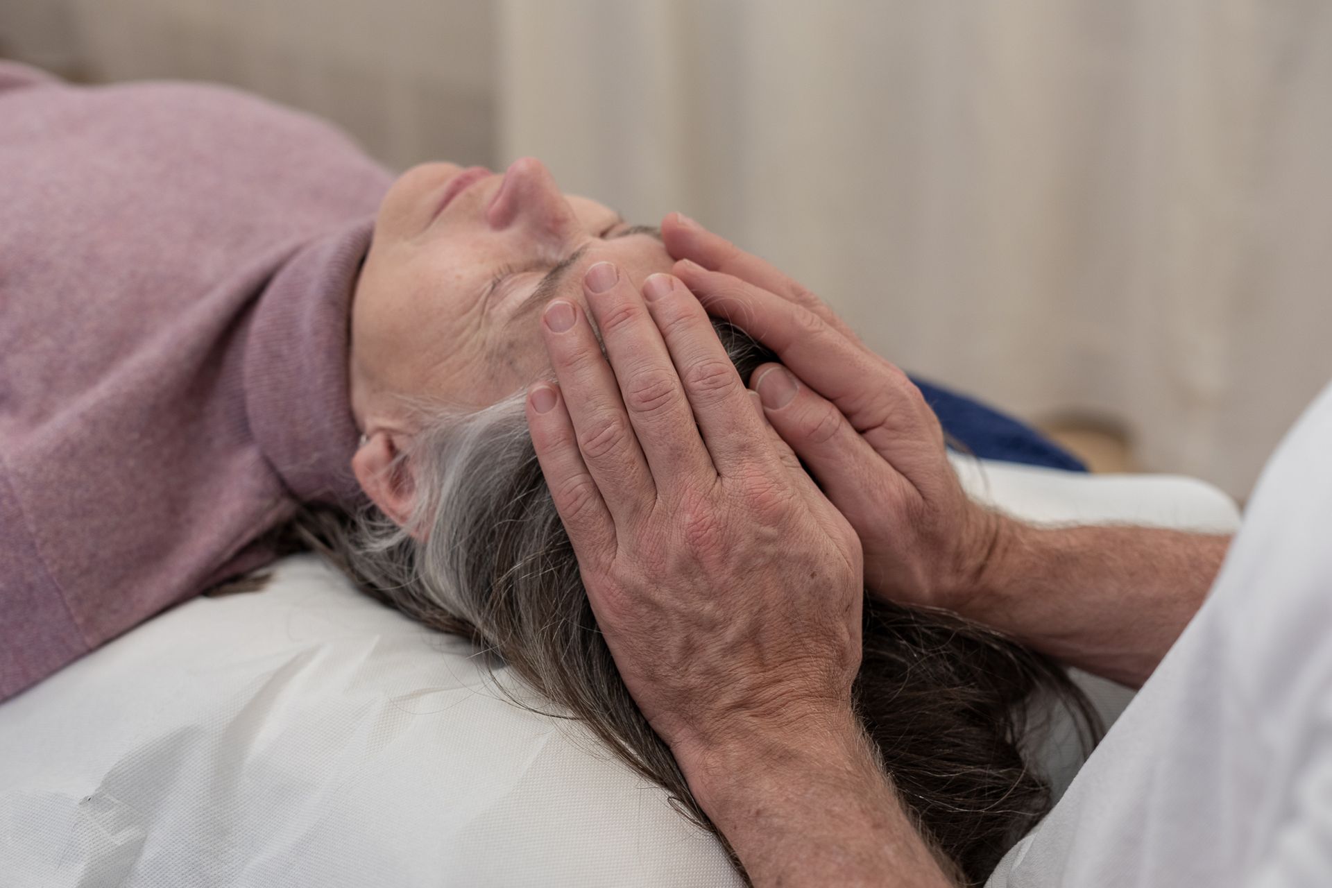 A woman is laying on a bed getting a head massage.