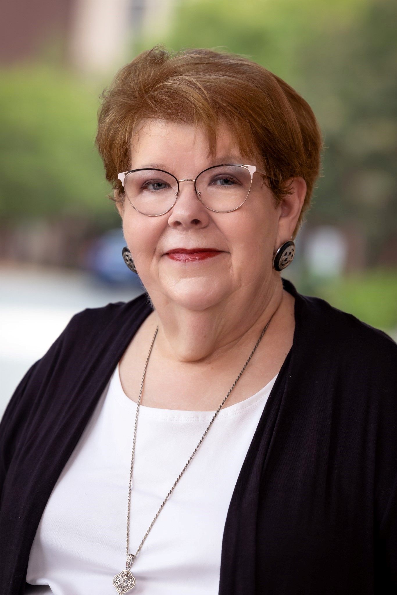 A woman is sitting at a desk with a laptop and a vase of flowers.