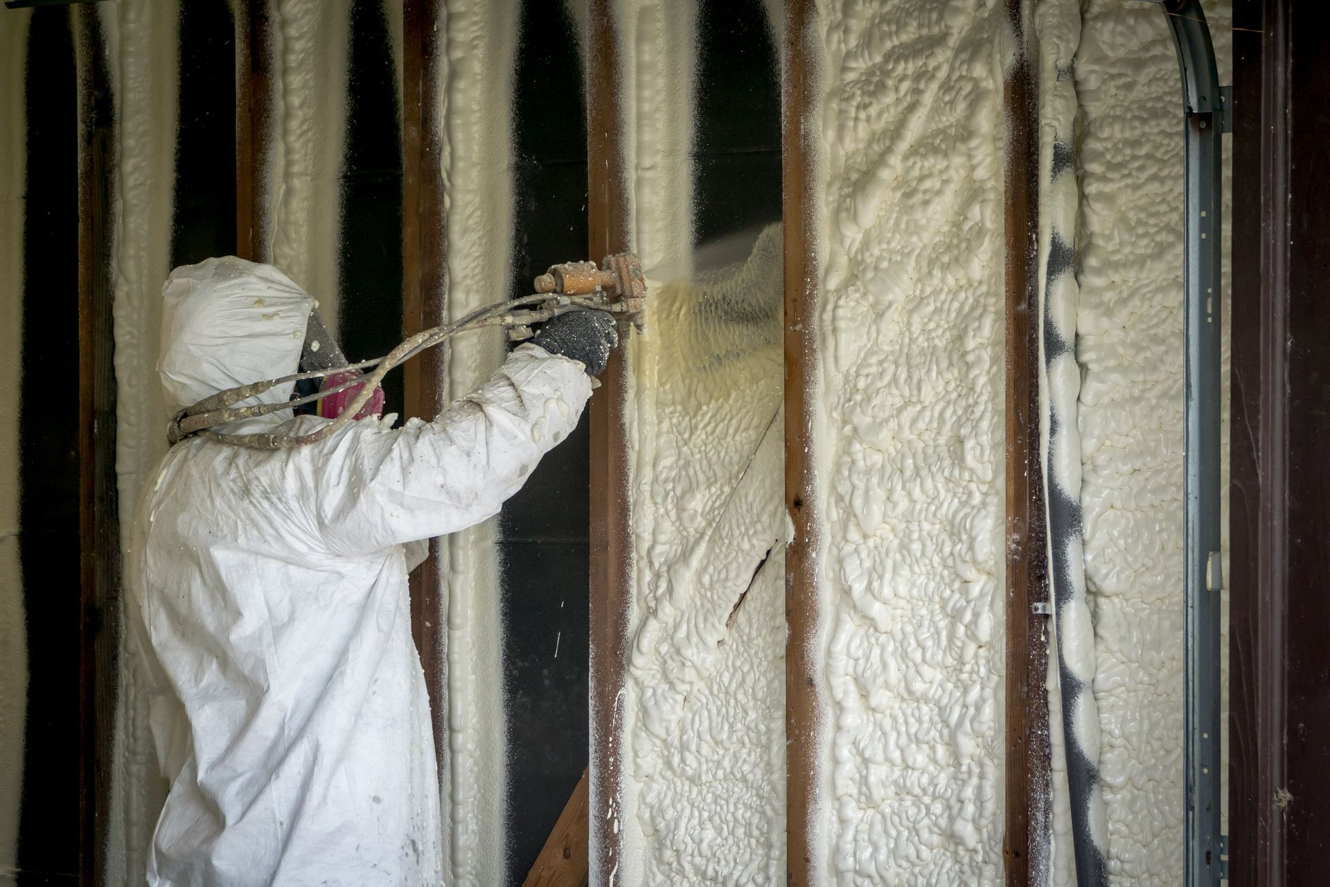 Worker sprays foam insulation into wall cavities during home renovation.