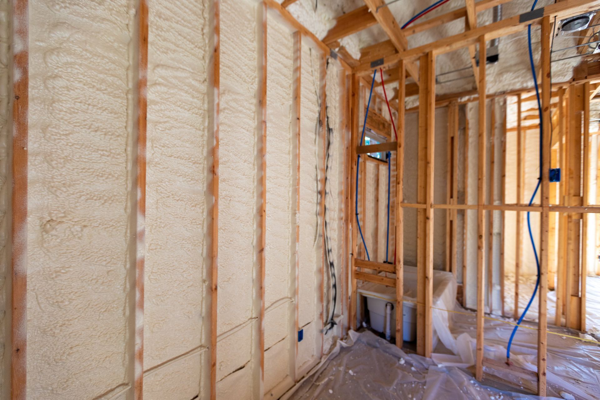 Interior of a house under construction with exposed wooden studs and spray foam insulation on the walls.
