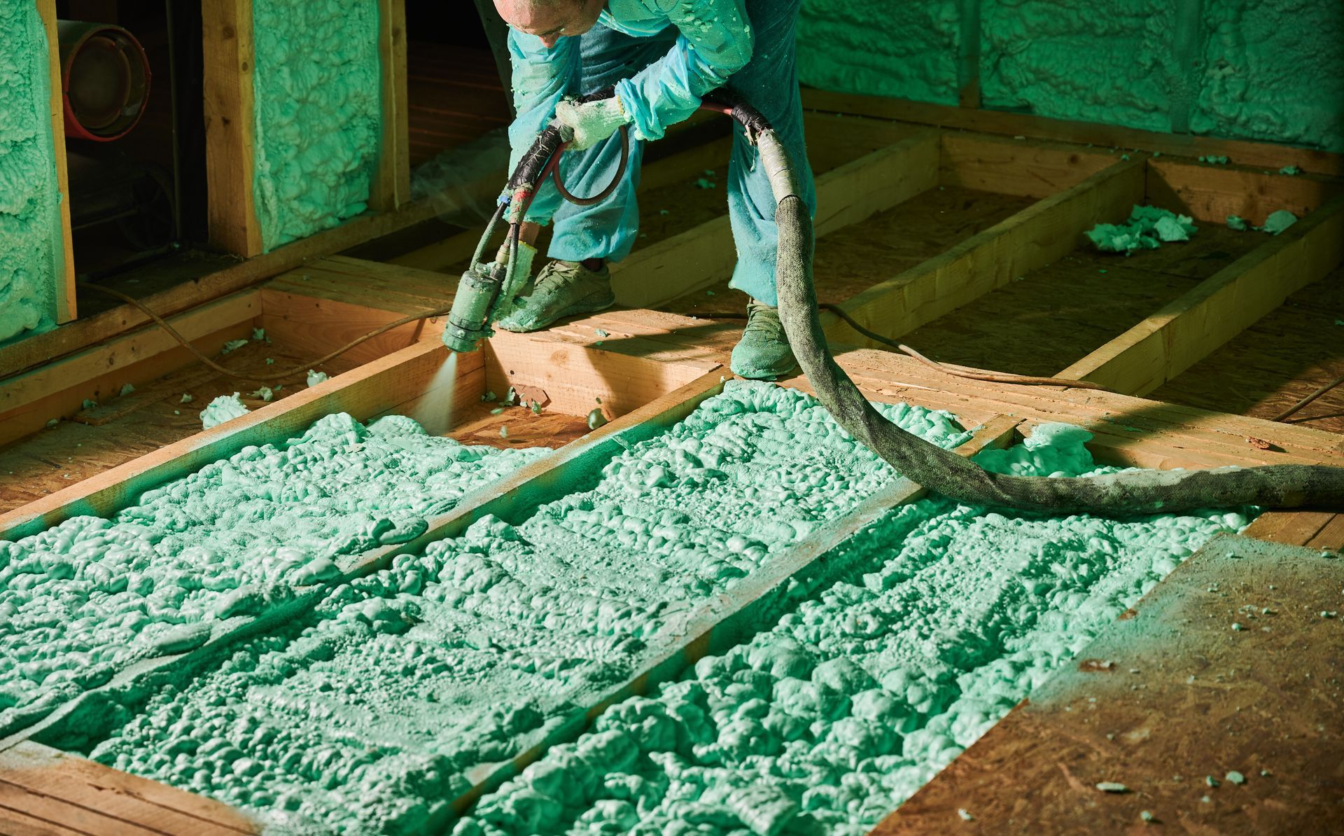 Technician applies spray foam insulation between floor joists inside a building during construction. Technician applies spray foam insulation between floor joists inside a building during construction.