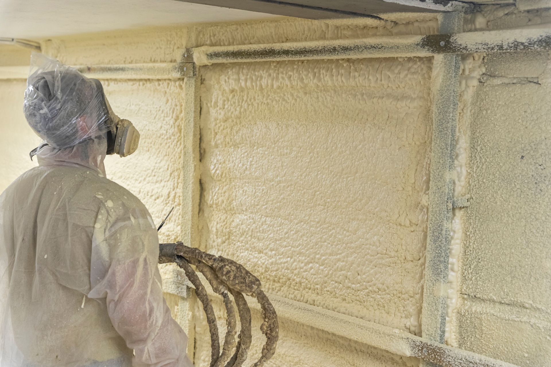 Worker in protective gear spraying foam insulation inside a wall cavity