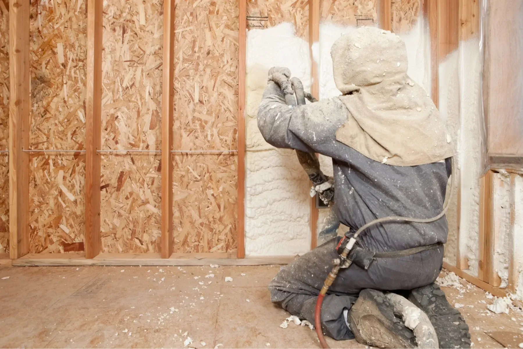 A man is spraying insulation on a wall in a room.