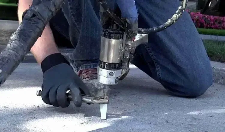 A man is kneeling down using a machine to spray concrete.