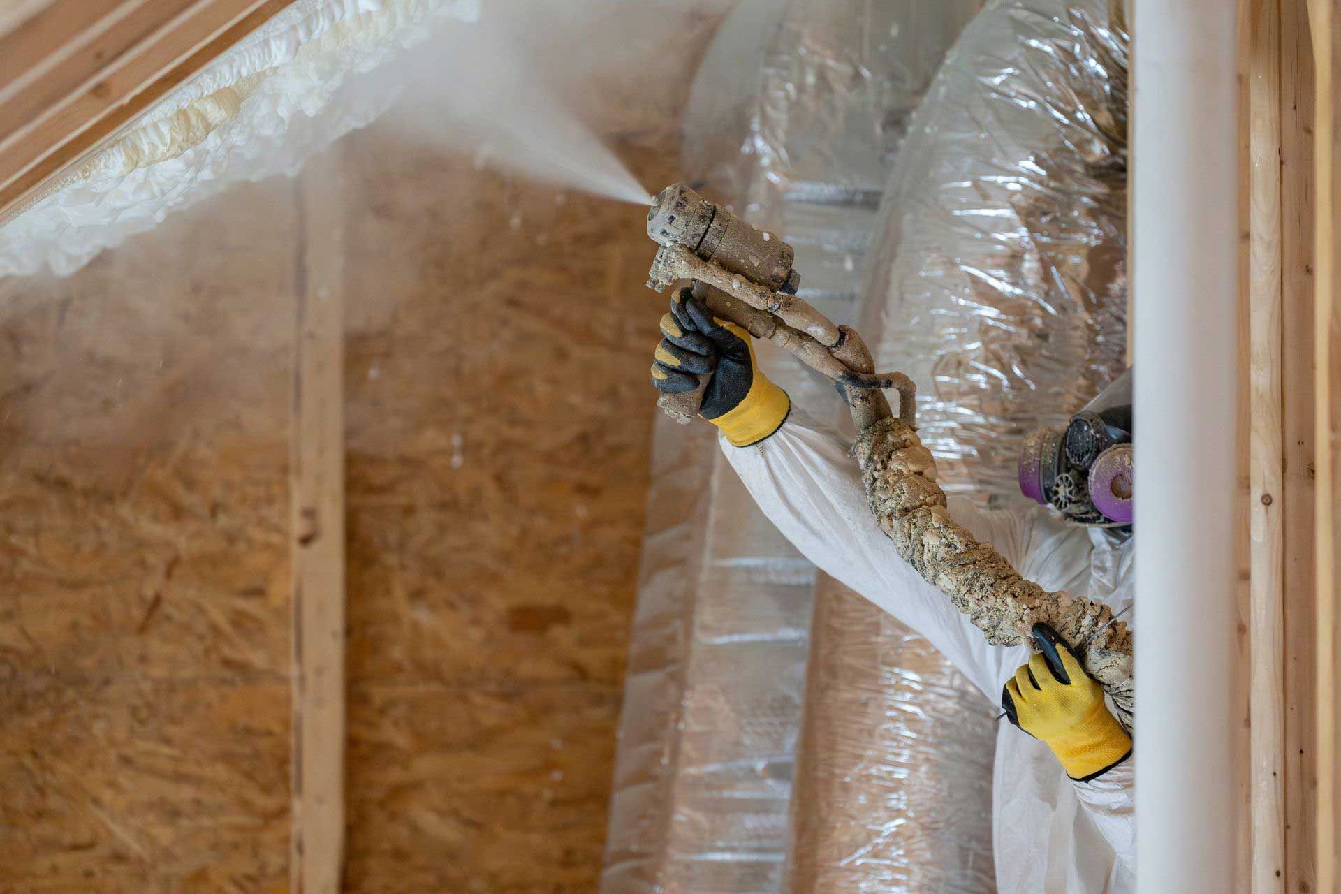 Commercial insulation contractor in protective gear using a mortar spraying equipment.