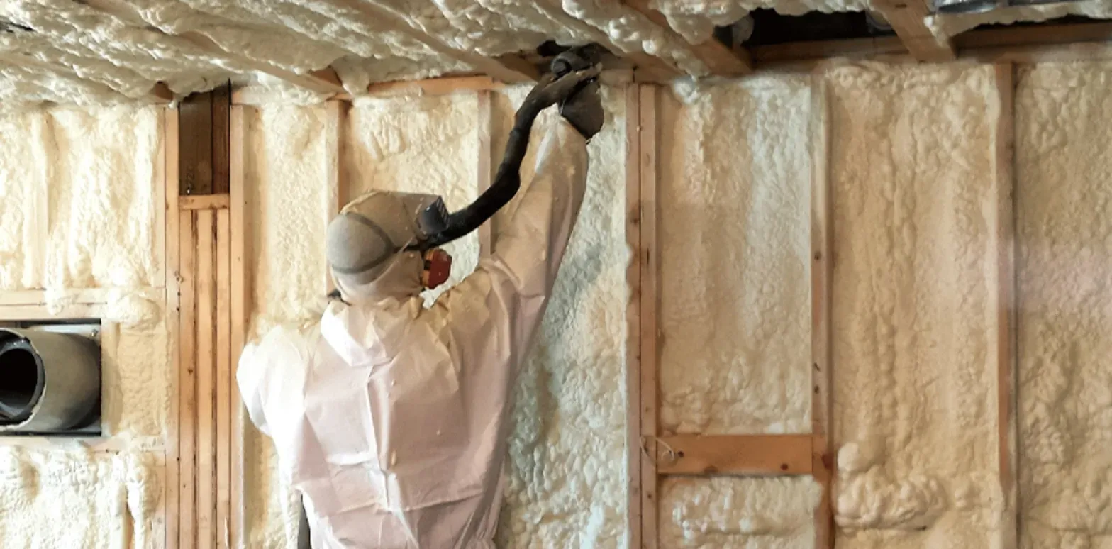 A man is spraying insulation on the ceiling of a house.