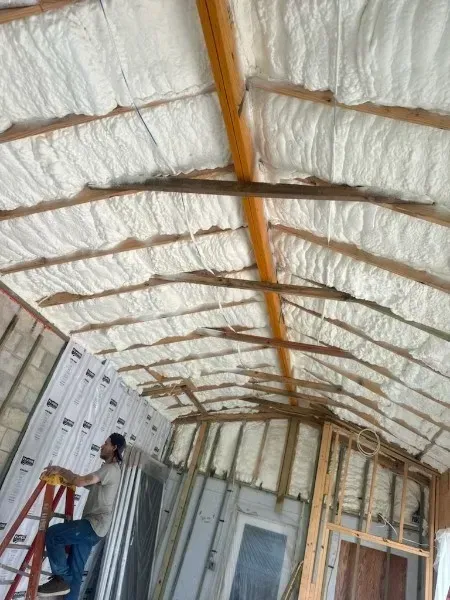 A man is standing on a ladder in a room with foam insulation on the ceiling.