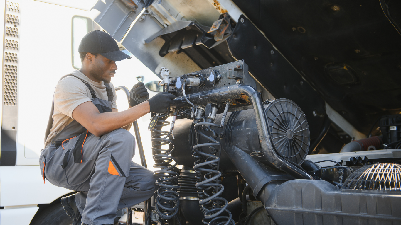 Mechanic inspecting a truck engine with a wrench; outdoors, wearing work overalls.