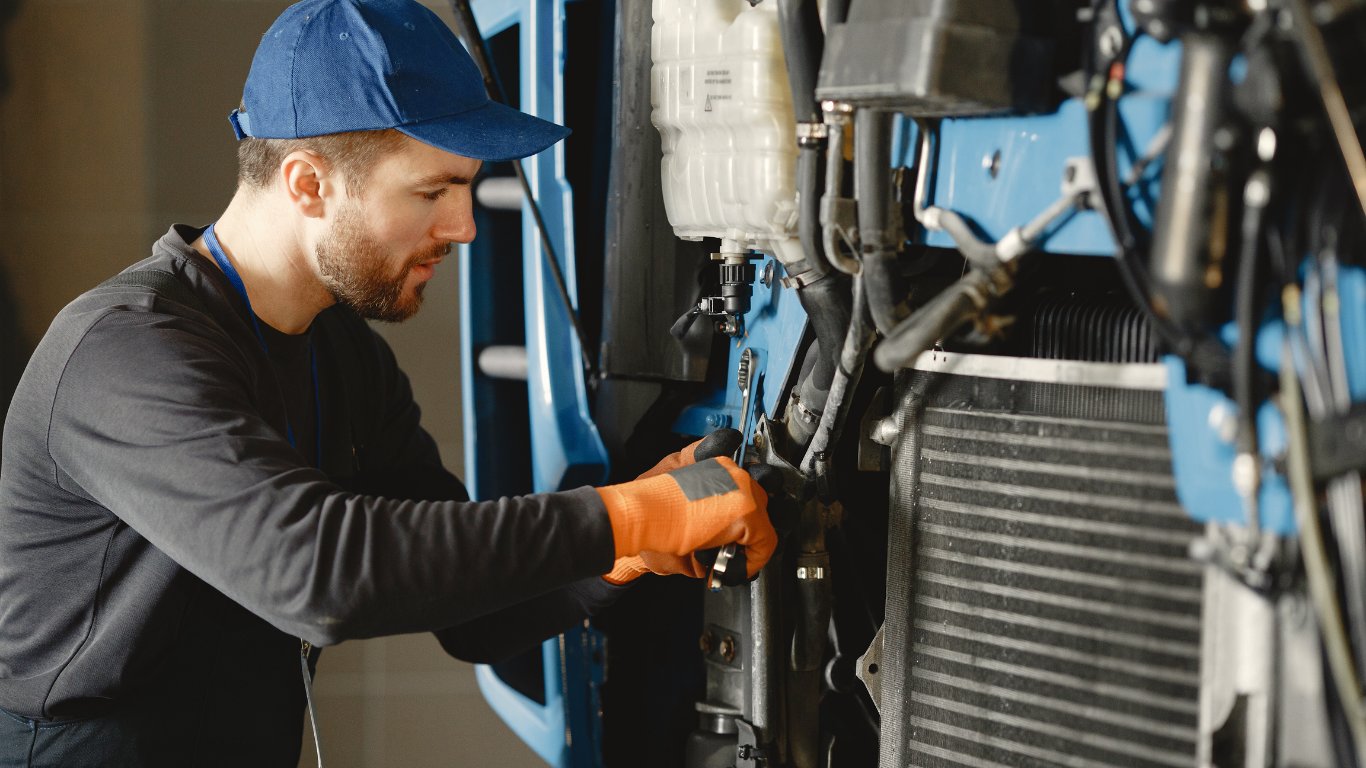 Mechanic in blue cap and orange gloves working on a blue vehicle in a shop.