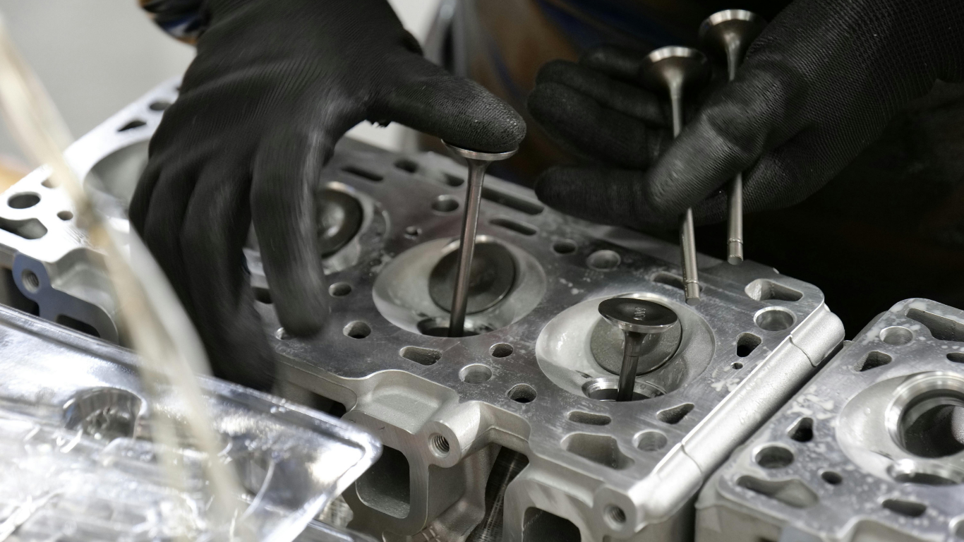 Hands in black gloves inserting engine valves into a cylinder head.