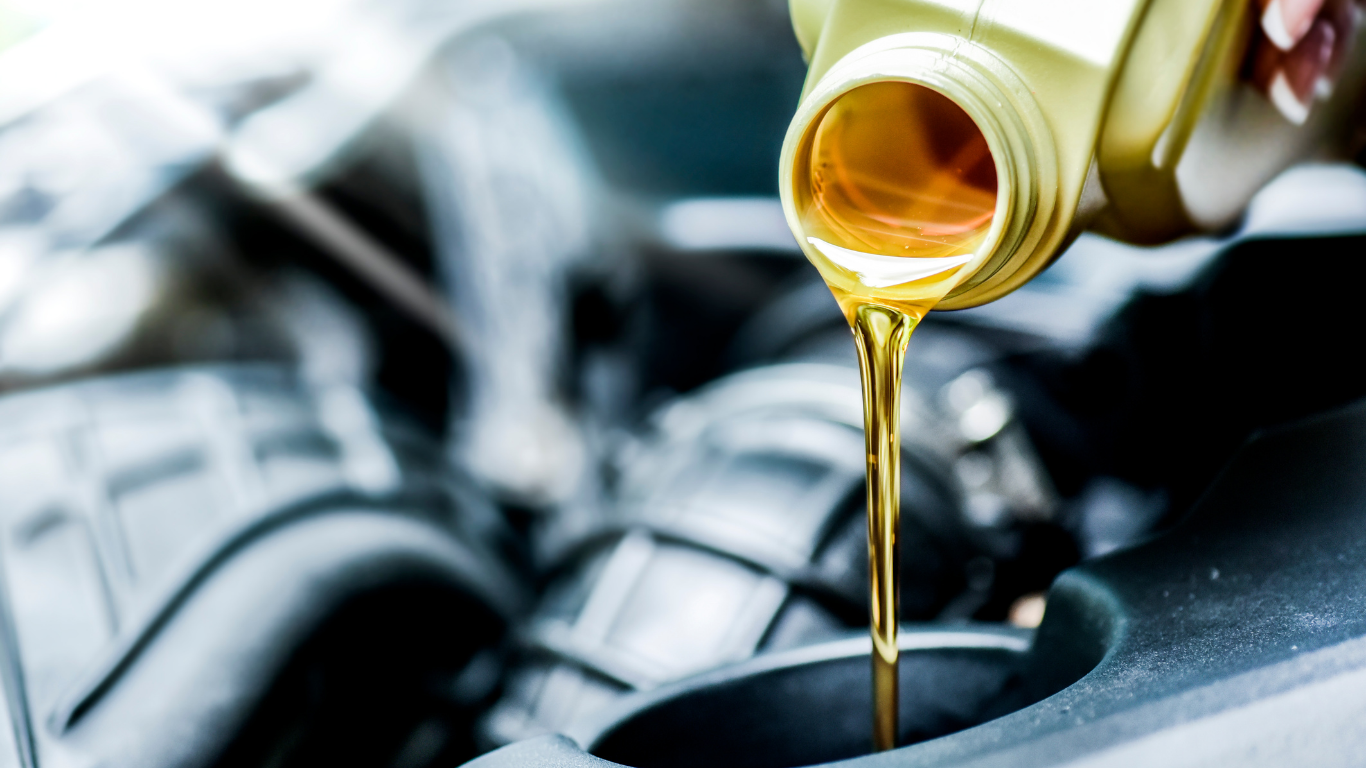 Oil being poured into a car engine, with the bottle and oil a golden color.