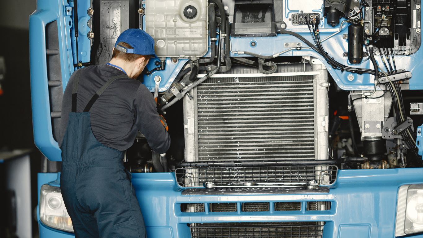Mechanic in blue coveralls working on a large, blue truck engine.