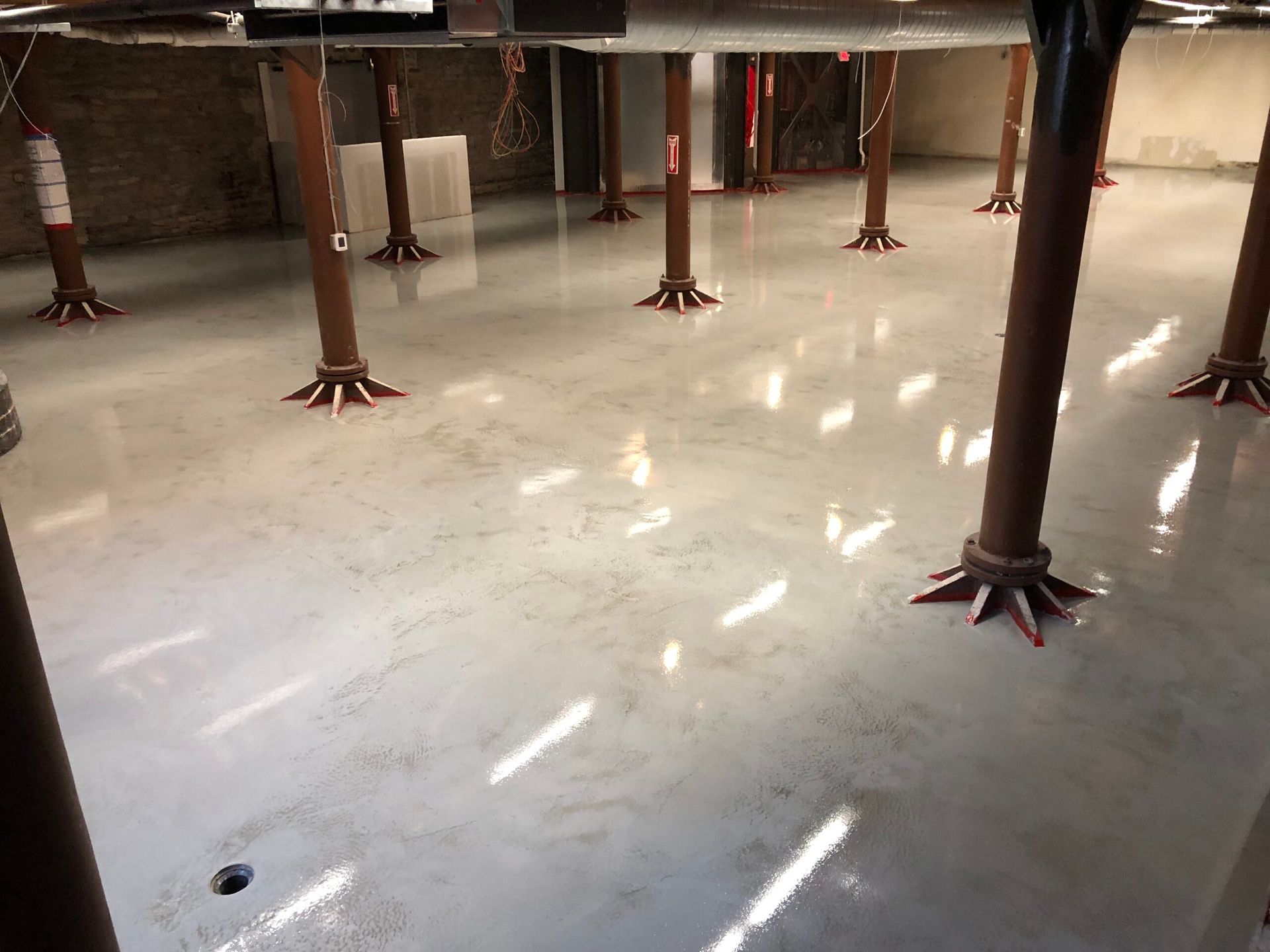 Shiny concrete floor in an industrial space with metal support legs and bright light reflections.