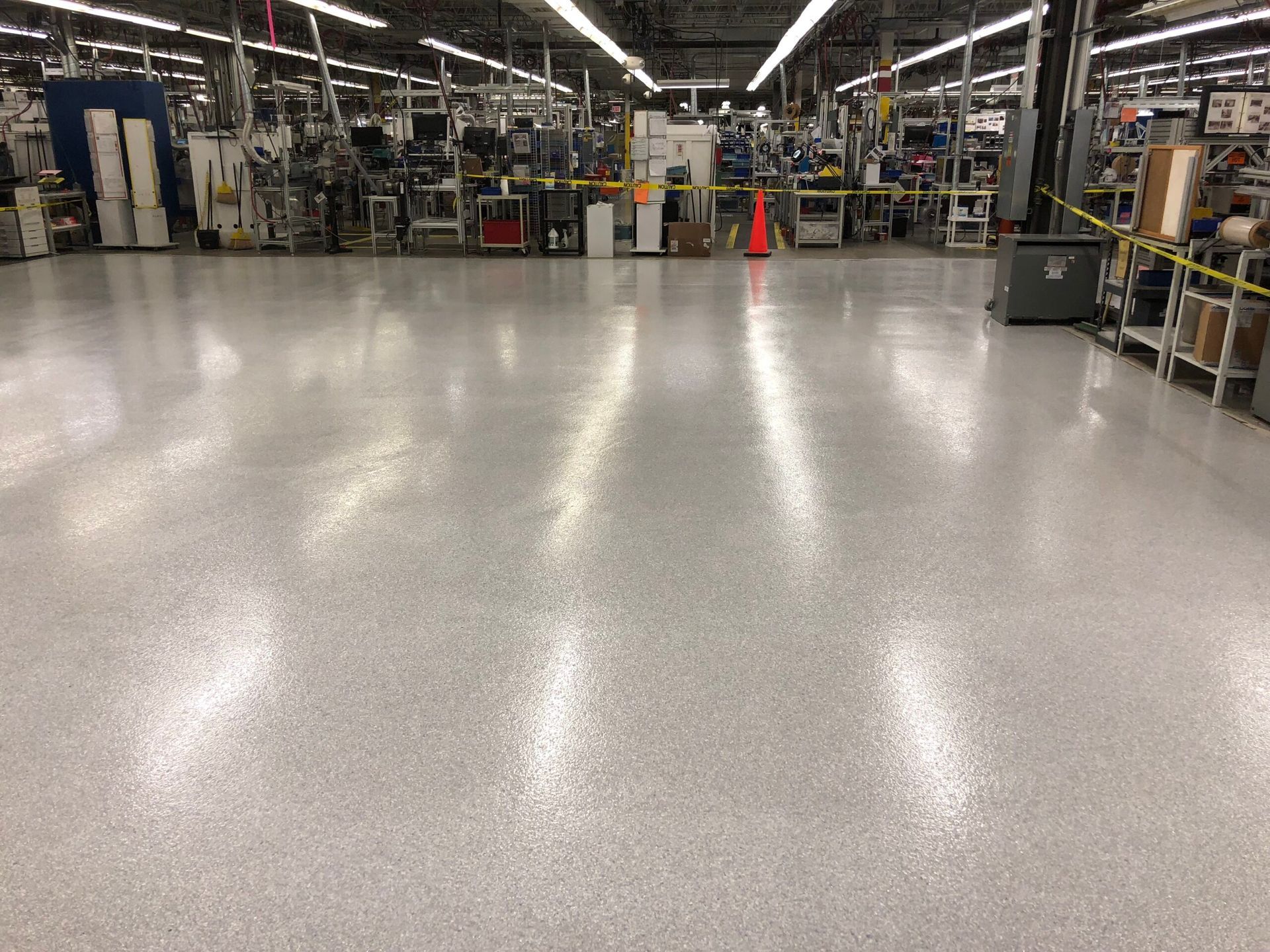 Empty factory floor with polished concrete, workstations along the sides, and an orange cone in the center.