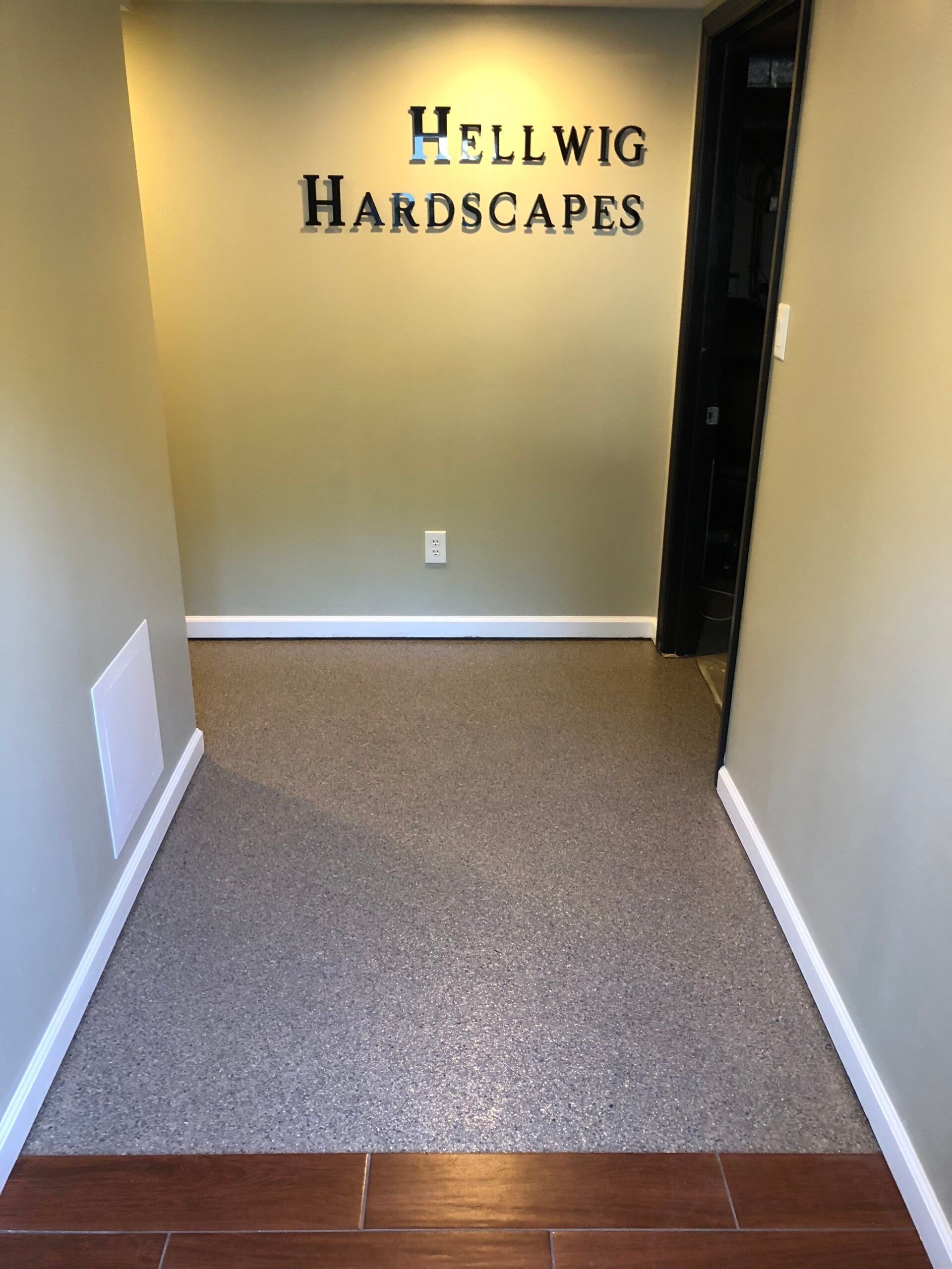 Empty office entryway with beige carpet leading to a wall sign reading “Hellwig Hardscapes.”