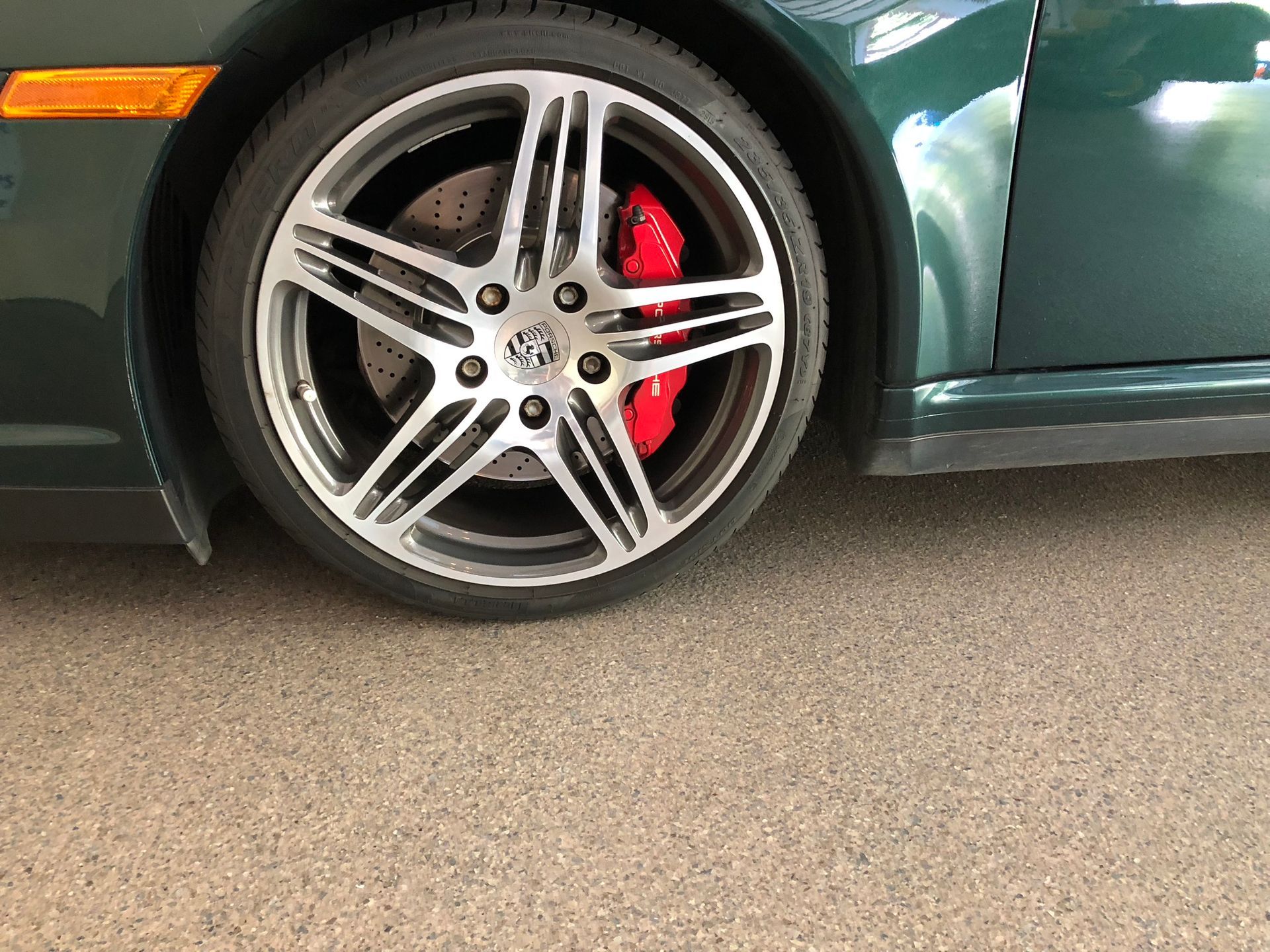 Close-up of a green car’s front wheel with silver alloy rim and red brake caliper.