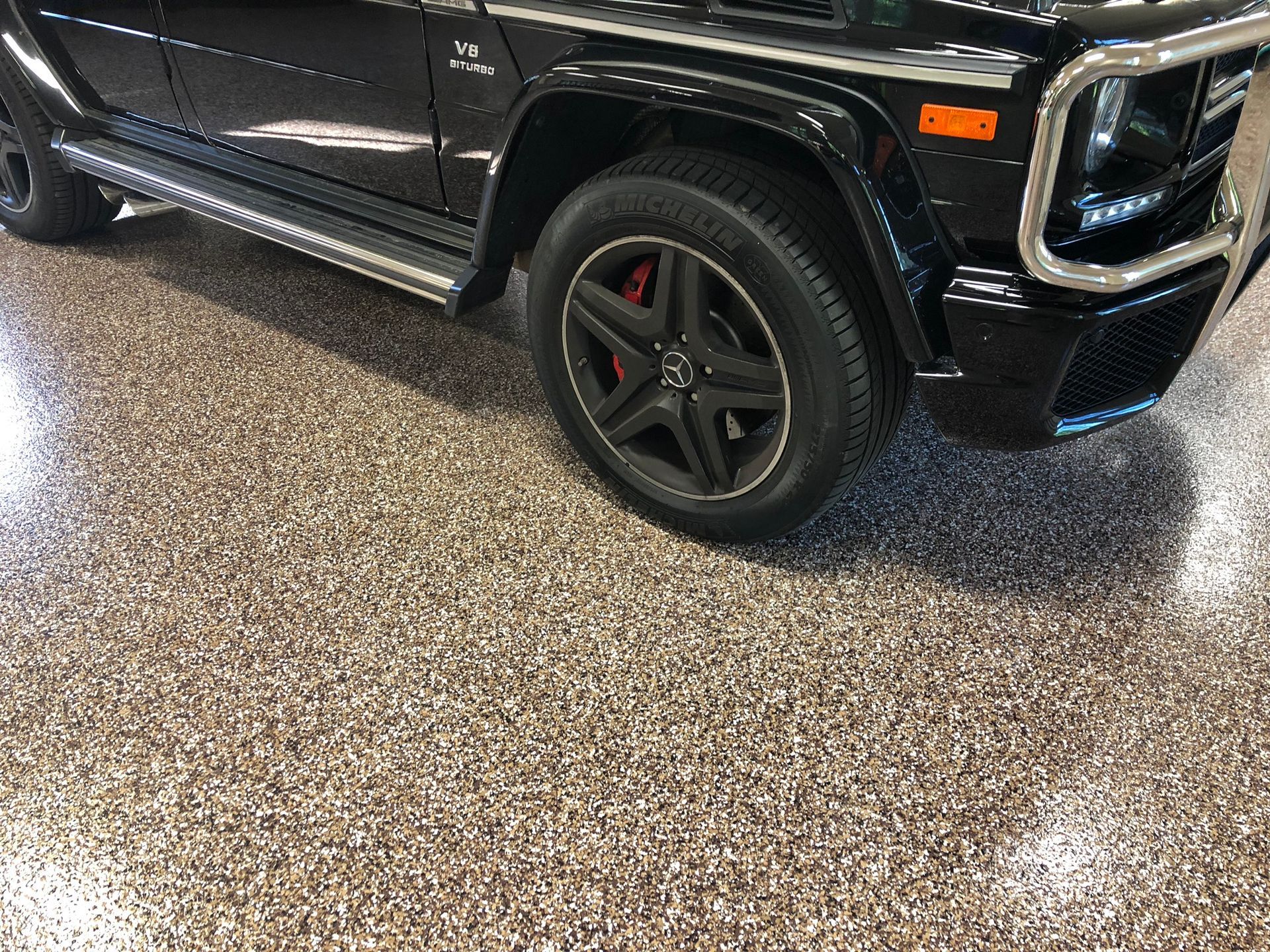 Black SUV parked on a speckled garage floor, showing the front side and wheel.