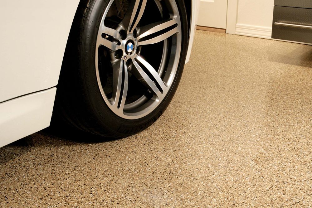Close-up of a car wheel and tire on a speckled garage floor beside a white vehicle body