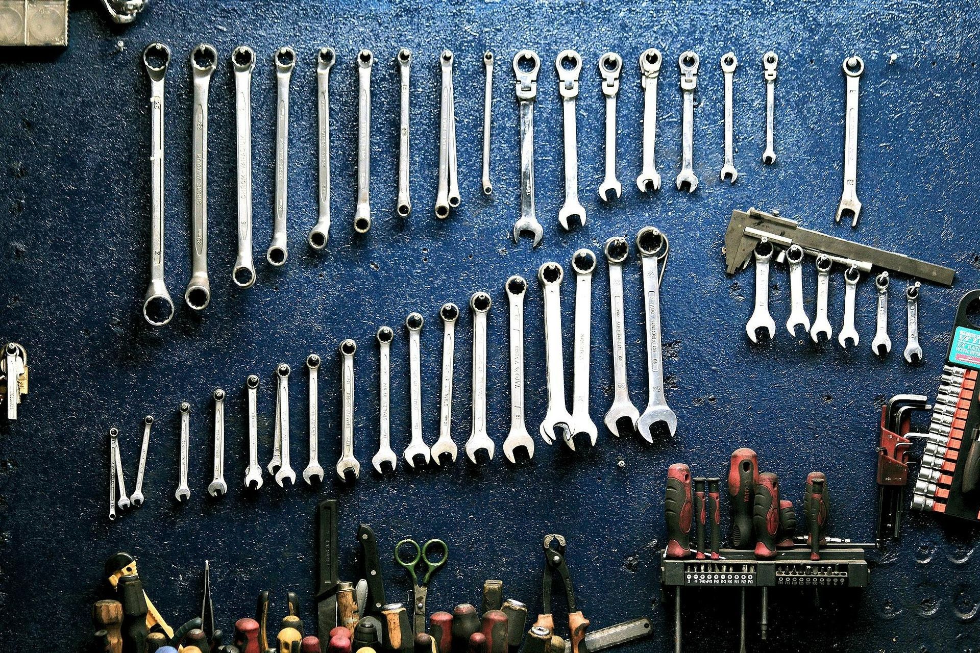 Rows of chrome wrenches and hand tools arranged on a blue workshop wall