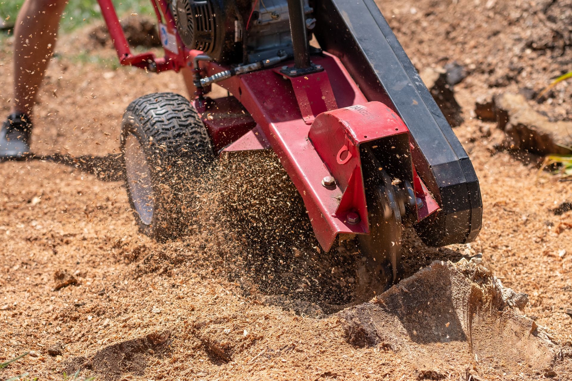 Red garden tiller digging into dry soil, kicking up dirt